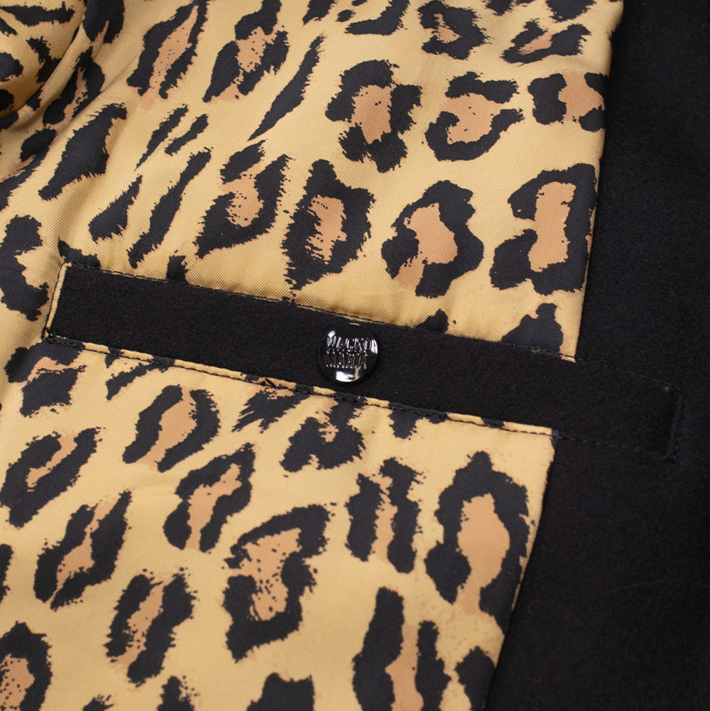 Interior studio close-up of the Wacko Maria Leather Varsity Jacket, showcasing the signature silky gold and black leopard-print fabric lining, an interior welt pocket with black fabric trim, and an embossed black branded button closure.