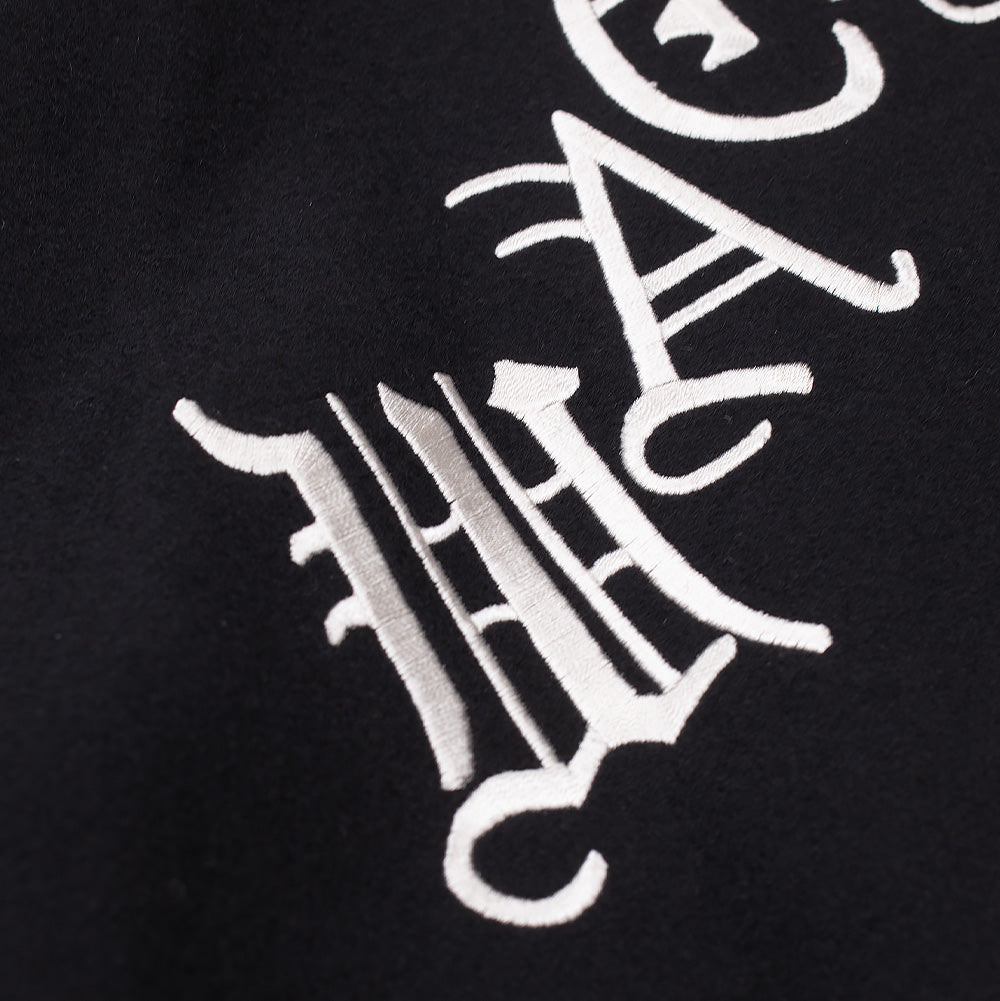 Extreme macro close-up of the rear embroidery on the Wacko Maria Leather Varsity Jacket, showcasing the heavy white thread satin stitching and intricate line definition of the gothic lettering on the premium black wool melton shell.