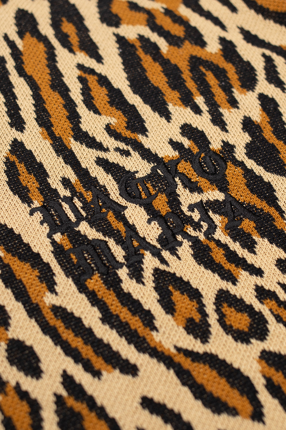 Wacko Maria embroidered logo detail on leopard knit polo shirt, black chest embroidery on beige animal print knit, showcasing luxury streetwear design and Tokyo aesthetics