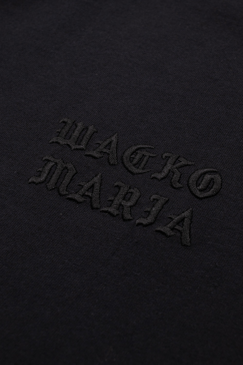 Detailed macro shot of the black tonal embroidered Wacko Maria Gothic font logo on the chest.