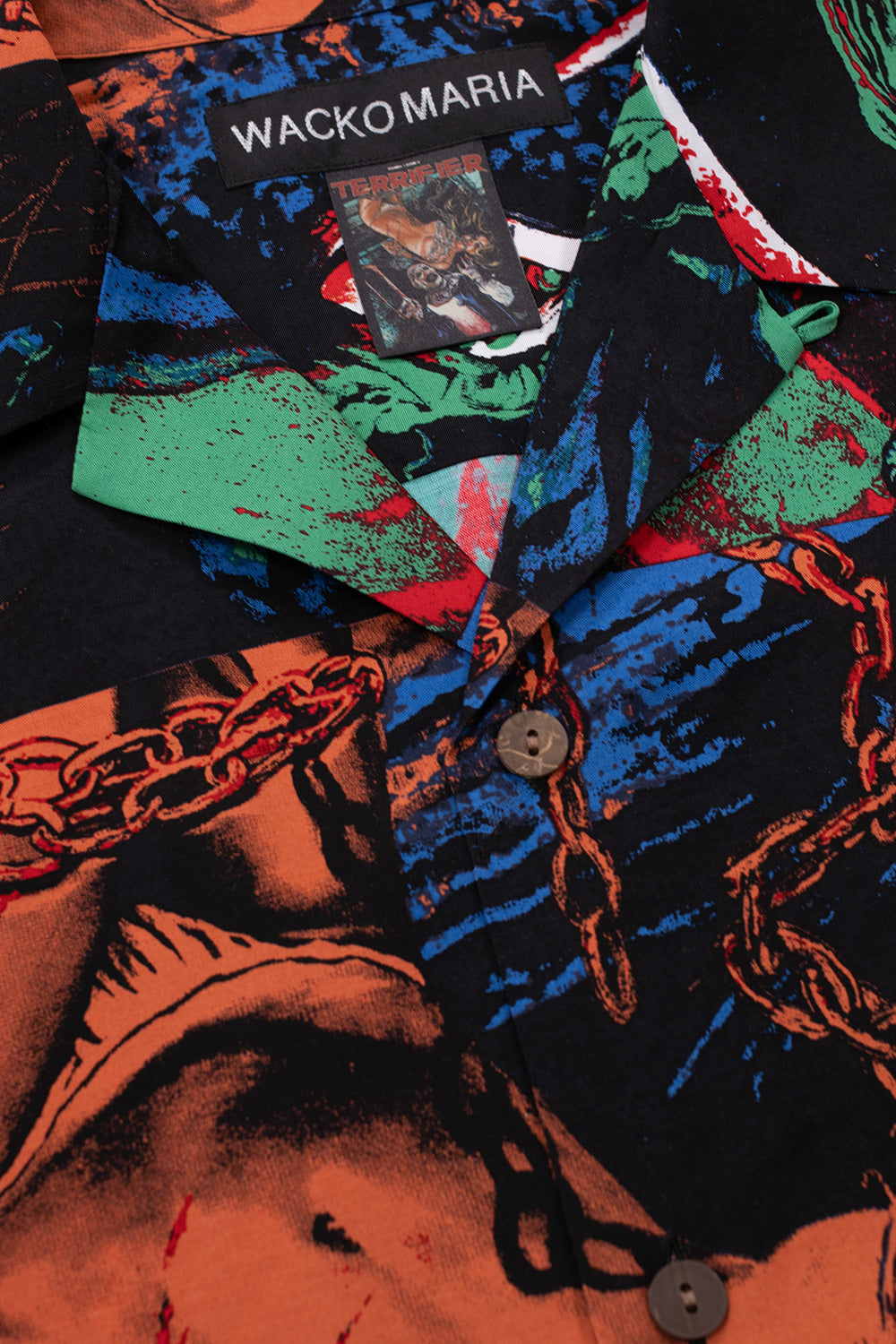 Close-up Wacko Maria x Terrifier shirt collar with branded label and Terrifier artwork tag, premium rayon fabric, bold all-over horror movie print with button-up design