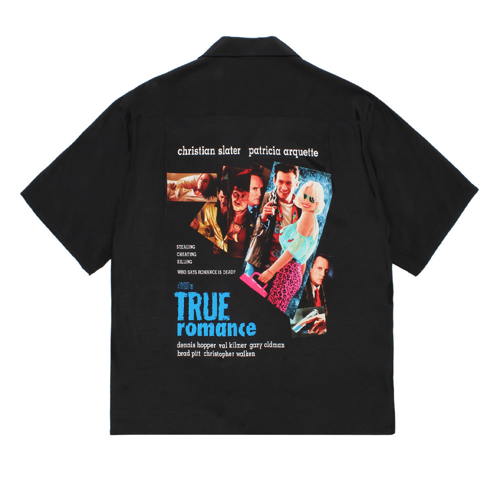 Back studio flat lay view of the Wacko Maria x True Romance Short Sleeve Hawaiian Shirt in solid black rayon, showcasing the straight hem and camp collar silhouette centered by a large graphic print featuring a colorful movie character collage of Christian Slater, Patricia Arquette, and the ensemble cast alongside blue and white typography.
