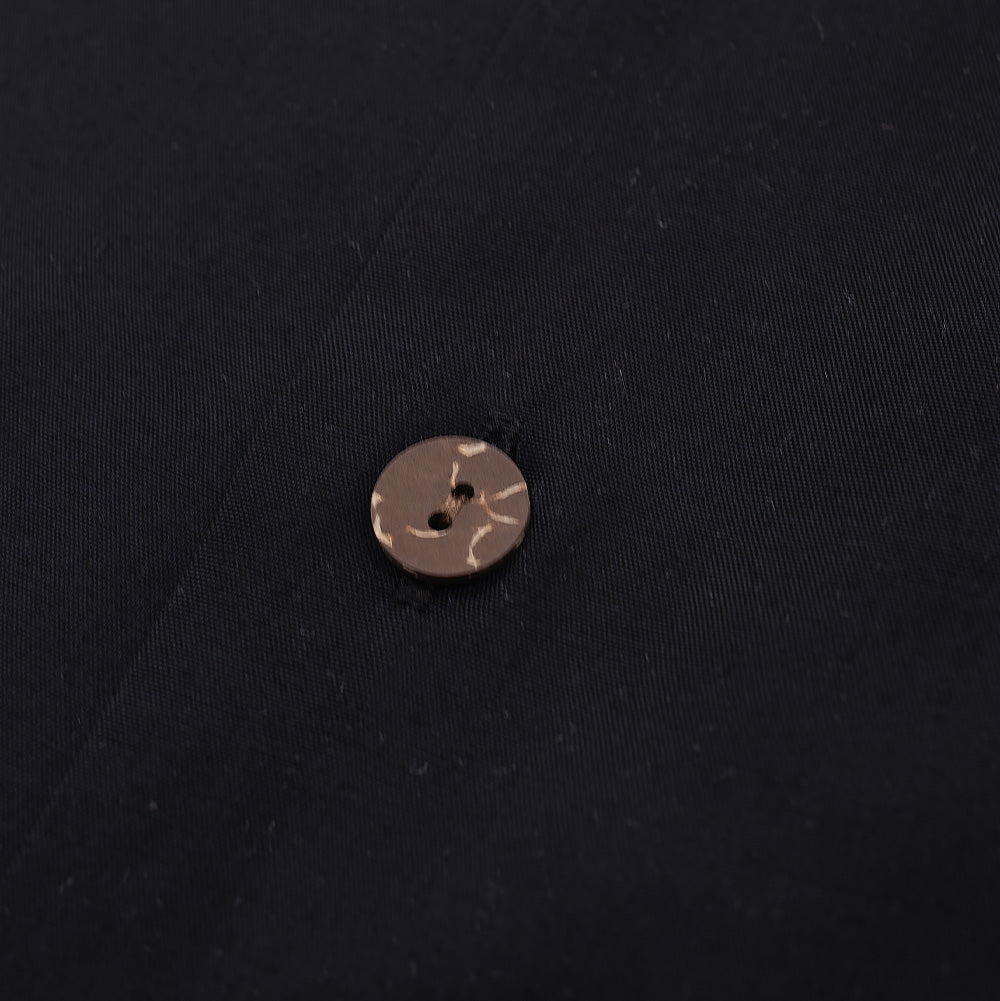 Extreme macro close-up of a front button on the black Wacko Maria x True Romance Hawaiian Shirt, showing the organic wood grain texture and light brown marbling of the two-hole fastener stitched securely to the black placket.