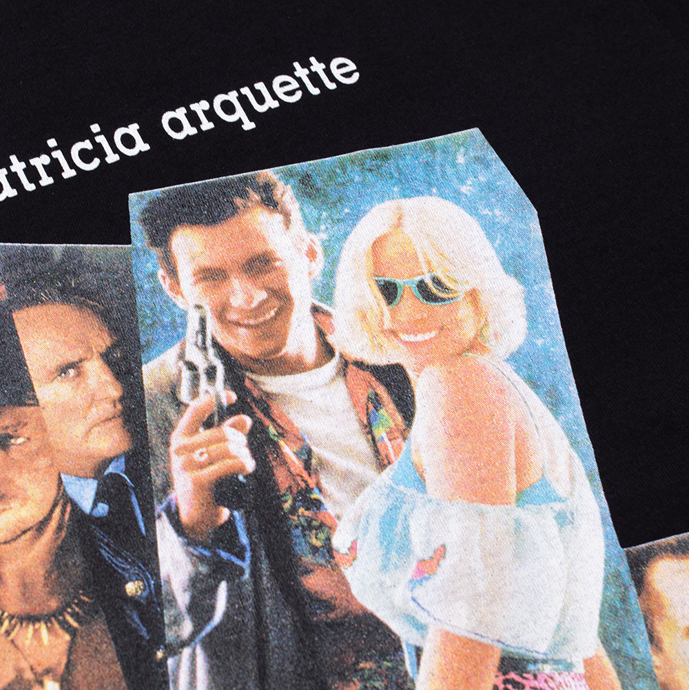 Detailed macro studio close-up of the front chest graphic on the Wacko Maria x True Romance T-Shirt, focusing on the vintage halftone screen print depicting Clarence and Alabama Whitman in retro sunglasses and leopard print beneath the white printed actors' names on heavyweight black cotton jersey.